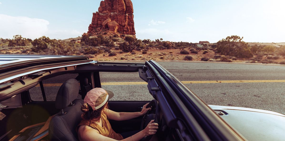 Frau im Cabrio vor roter Felslandschaft im Arches Nationalpark in den USA
