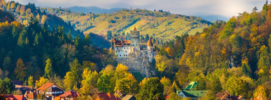Herbstlich gefärbte Wälder und sanfte Hügel umgeben ein Dorf in der rumänischen Landschaft Transelvaniens.