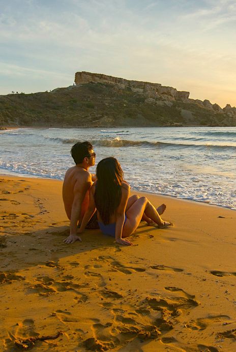 Ein Paar beobachtet den Sonnenuntergang am Strand von Ghajn Tuffieha Bay, Malta