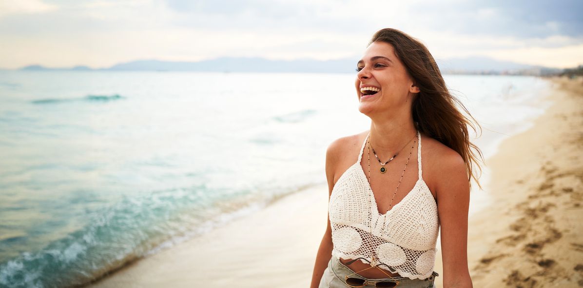 Eine Frau geht lachend am Strand spazieren