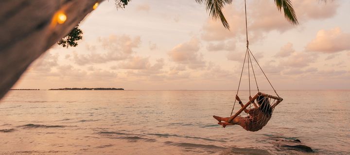 Frau auf Schaukel unter einem Baum vor dem Meer
