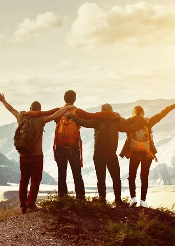 Wandergruppe steht auf Berggipfel und blickt über sonnige Täler