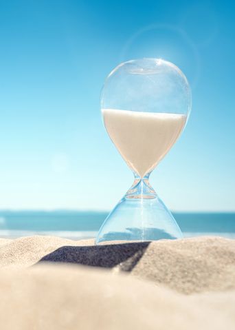 Sanduhr im Sand mit Meer im Hintergrund