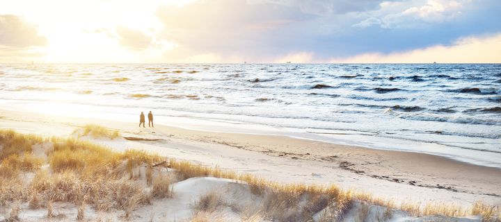 Spaziergänger gehen am Ostseestrand entlang zwischen Dünen und Meereswellen