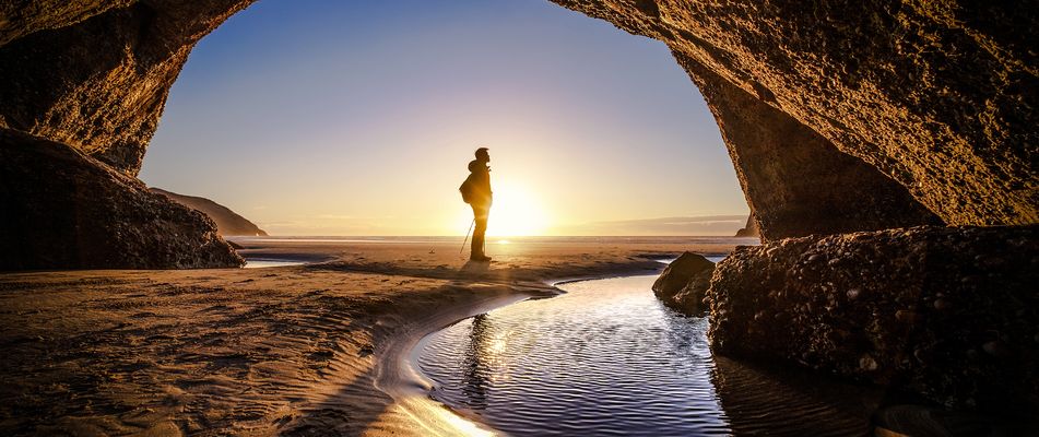 Mann steht am Höhleneingang vor dem Sonnenuntergang