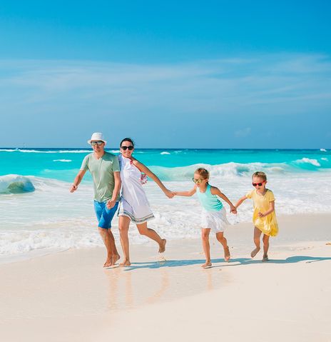 Eine Familie mit zwei Kindern läuft fröhlich durch die Wellen am Strand