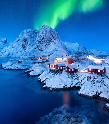 Blick auf verschneite Berge, rote Häuser und Polarlichter am Himmel