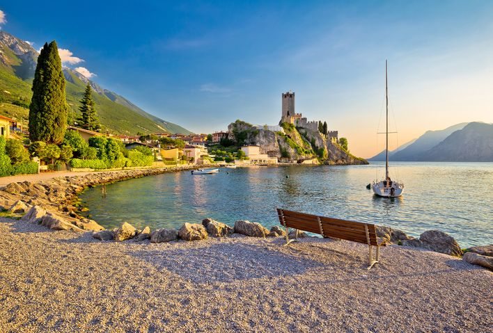 Strand in Malcesine am Gardasee mit Blick auf die Scaligerburg und Segelboot bei Sonnenuntergang