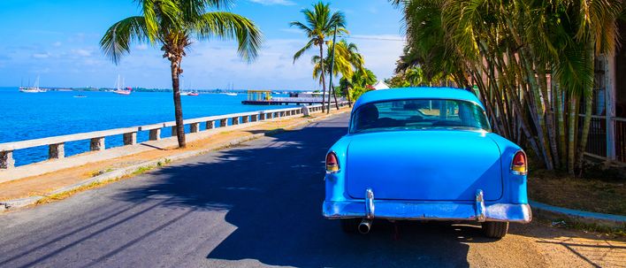 Blauer Oldtimer auf einer Küstenstraße mit Palmen umsäumt in Varadero auf Kuba
