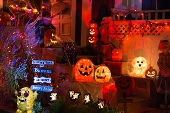 Leuchtende Kürbisse und Halloween-Deko verteilt um Hauseingänge bei Dunkelheit 