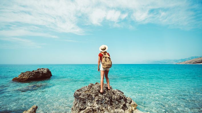 Frau steht auf einem Felsen und schaut auf das Meer