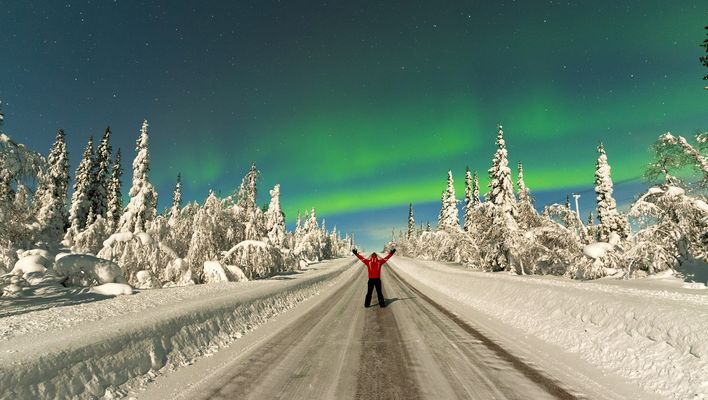Mann steht im Schnee bei Nordlichtern in Skandinavien