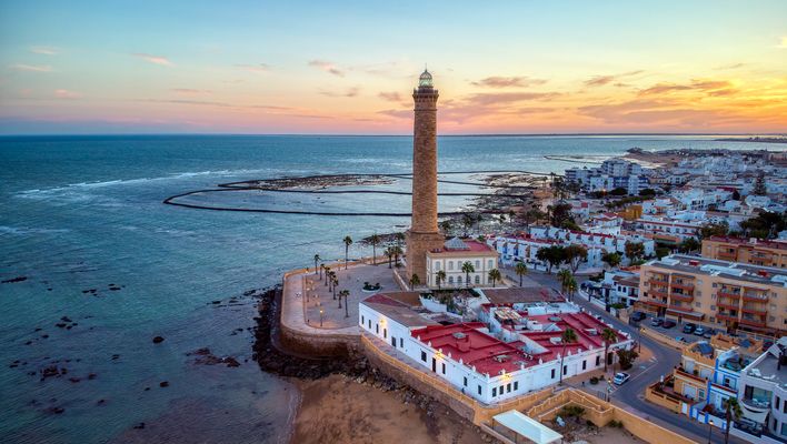 Luftaufnahme der Atlantikküste von Cádiz mit Leuchtturm, Stadtmauern und farbigem Abendhimmel