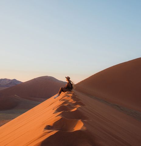 Frau sitzt in der Wüste im Namib Naukluft Nationalpark in Namibia und genießt den Ausblick