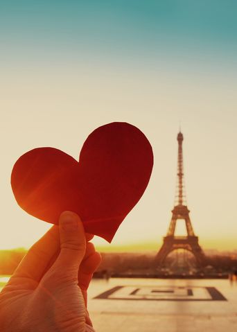 Person hält Herz aus Papier vor den Eifelturm in Paris
