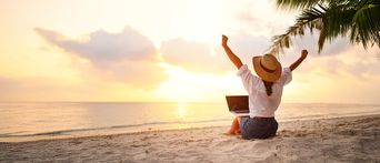 Frau sitzt am Strand mit einem Laptop und freut sich