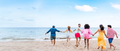 Gruppe junger Leute läuft Hand in Hand am Strand Richtung Meer