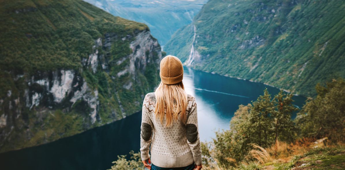 Eine Frau mit Mütze schaut auf den Geiranger Fjord hinab in Norwegen