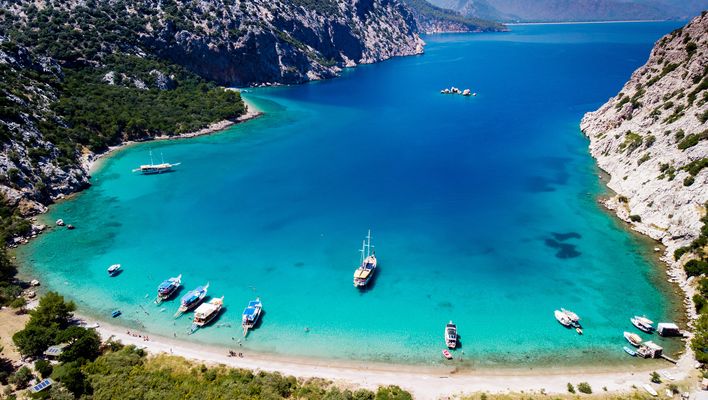 Blick auf die Bucht von Antalya mit steilen Felsen, türkisfarbenem Wasser und Badebooten