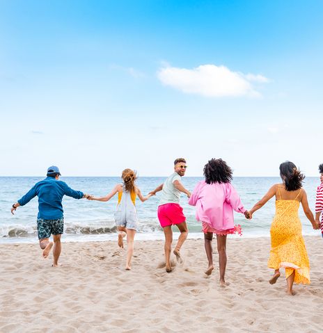 Gruppe junger Leute läuft Hand in Hand am Strand Richtung Meer