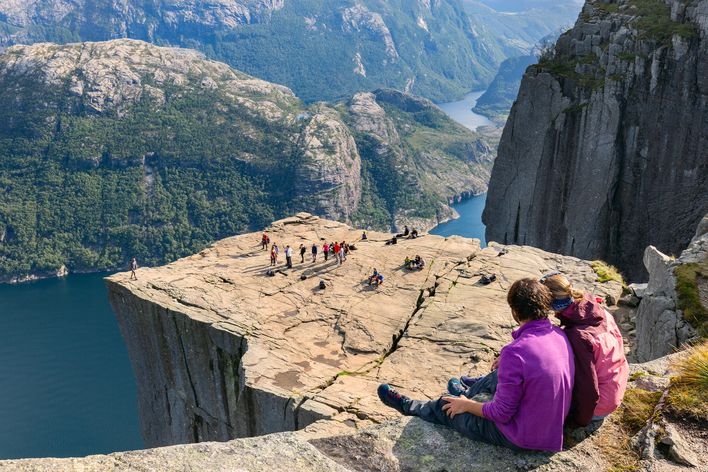 Zwei Frauen sitzen auf Felsen und schauen auf das Preikestolen in Norwegen