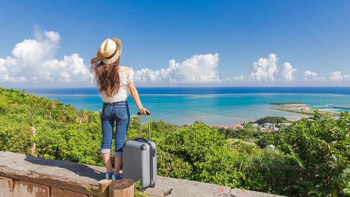 Frau mit Koffer blickt auf das weite Meer
