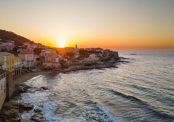 Seitlicher Blick auf den Strand mit Felsen und Häusern von Algajolo auf Korsika in Frankreich beim Sonnenuntergang