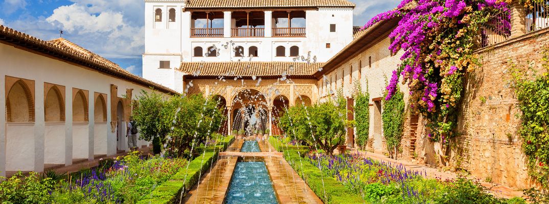Blühende Bougainvilleen und ein Wasserbecken schmücken die sonnigen Gärten des Generalife in Granada.