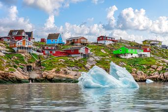 Bunte Häuser von Ilulissat direkt am Wasser mit treibenden Eisbergen