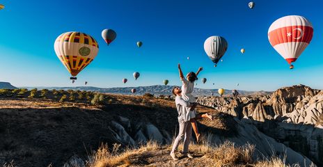 Frau mit ausgebreiteten Armen wird von Mann hochgehoben während sie die Heißluftballons über den Feenkaminen in Kappadokien in der Türkei bewundern