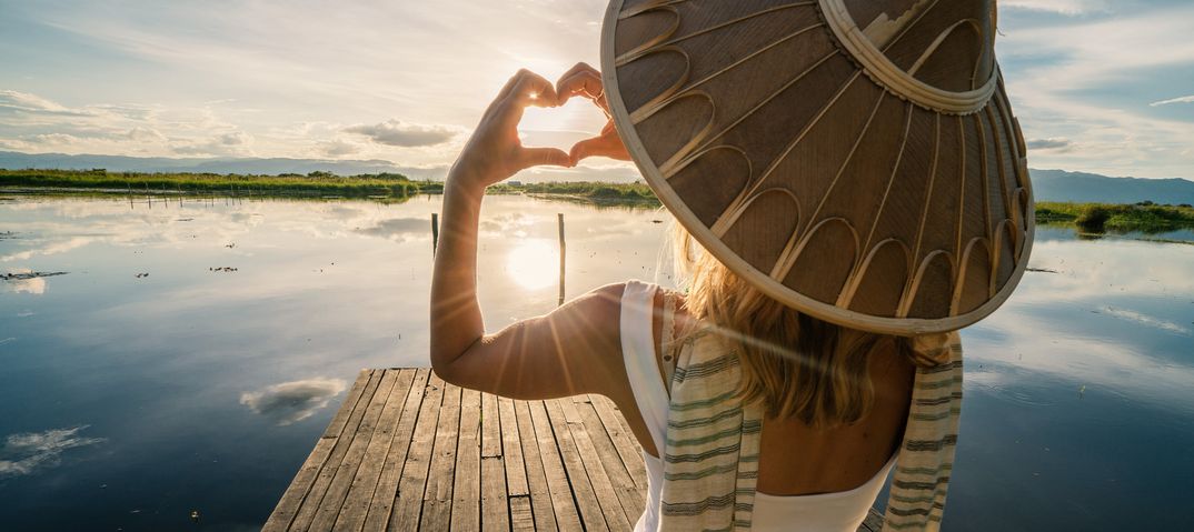 Frau formt mit ihren Händen ein Herz an einem See in Myanmar