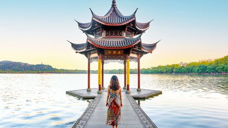Frau in rotem Kleid vor traditionellem Pavillon am Westsee in Hangzhou