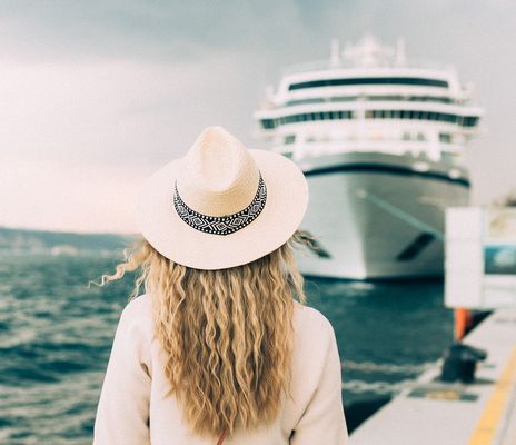 Frau mit Hut steht vor einem Kreuzfahrtschiff