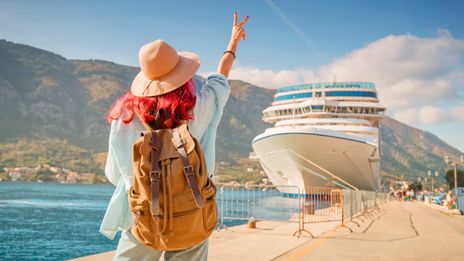 Frau steht mit Rucksack an Anlegestelle eines Kreuzfahrtschiffes