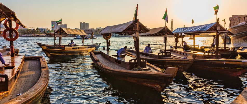 Blick auf traditionelle Holzboote im Hafen von Dubai mit Skyline