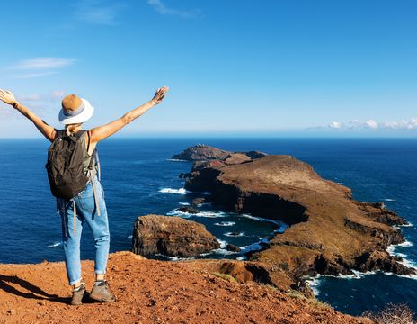 Eine Wanderin streckt auf einer felsigen Landzunge Madeiras die Arme über dem Atlantik aus