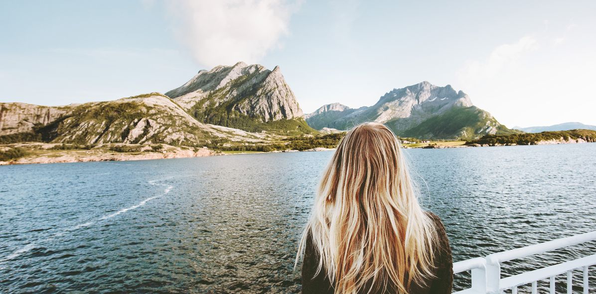 Eine Frau die an Bord eines Schiffes ist und auf Berge in Norwegen schaut