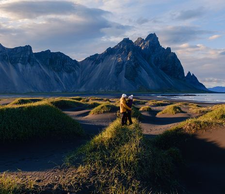 Paar in der Landschaft von Stokksnes auf Island bei Sonnenschein mit Dünen, Strand und Bergkulisse