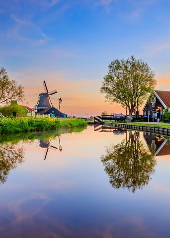 Idyllische Dorfkulisse mit Windmühle, Holzhäusern und spiegelndem Kanal in Zaanse Schans, Niederlande