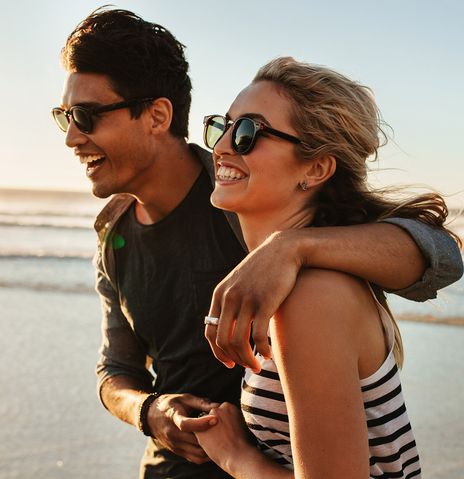 Junges fröhliches Paar spaziert gemeinsam am Meer entlang
