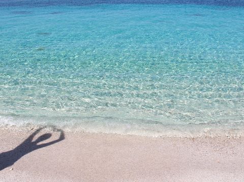 Mensch steht am kristallblauen Meer und macht ein Schattenbild mit Herz 