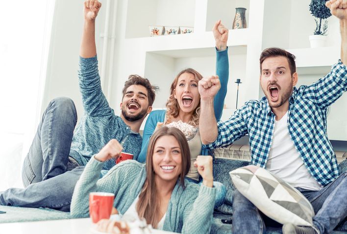 Gruppe von Freunden im Wohnzimmer jubelt