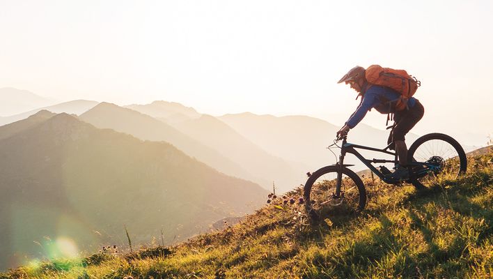 Mountainbiker fährt bergauf auf einem schmalen Trail bei Sonnenuntergang