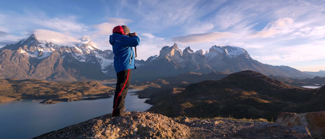 Ein Mann steht auf einem Felsen im Torres del Paine Nationalpark und fotografiert die markanten Berge im Hintergrund, Chile