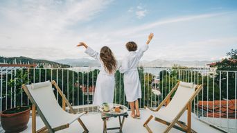 Zwei Frauen genießen den Ausblick von ihrem Hotel-Balkon auf einen Hafen