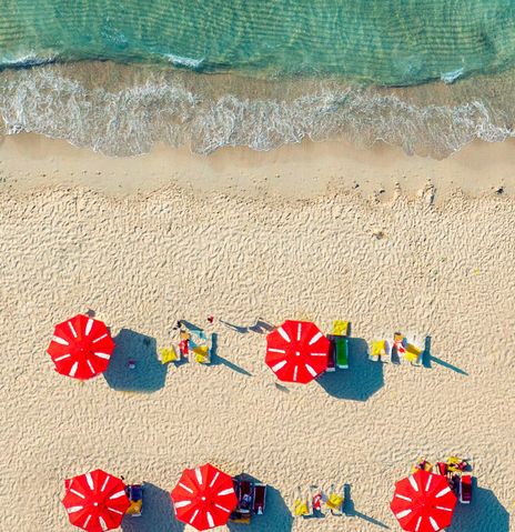 Luftaufnahme von roten Sonnenschirmen am weißen Sandstrand von Mykonos, Griechenland