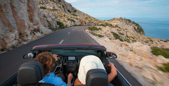 Personen fahren im Cabrio am Cap de Formentor eine Küstenstraße entlang, Blick aufs Meer