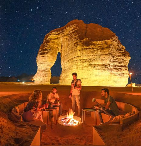 Wüstenlager bei Nacht mit Feuerstelle und beleuchteten Felsen in Saudi-Arabien