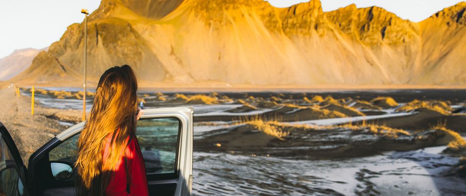 Frau in Rückansicht, die in Island aus einem Auto aussteigt und die Landschaft betrachtet