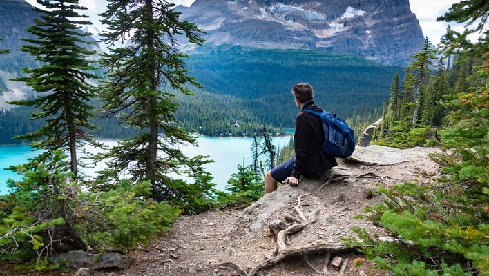 Wanderer mit Rucksack blickt auf türkisfarbenen Bergsee inmitten kanadischer Natur
